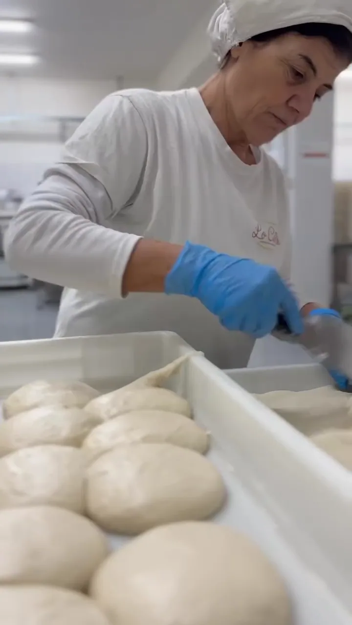 Una panettiera con guanti blu lavora i panetti di impasto su un vassoio