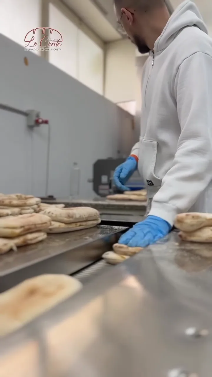 Un panettiere con guanti blu sistema i prodotti appena sfornati sul nastro del laboratorio