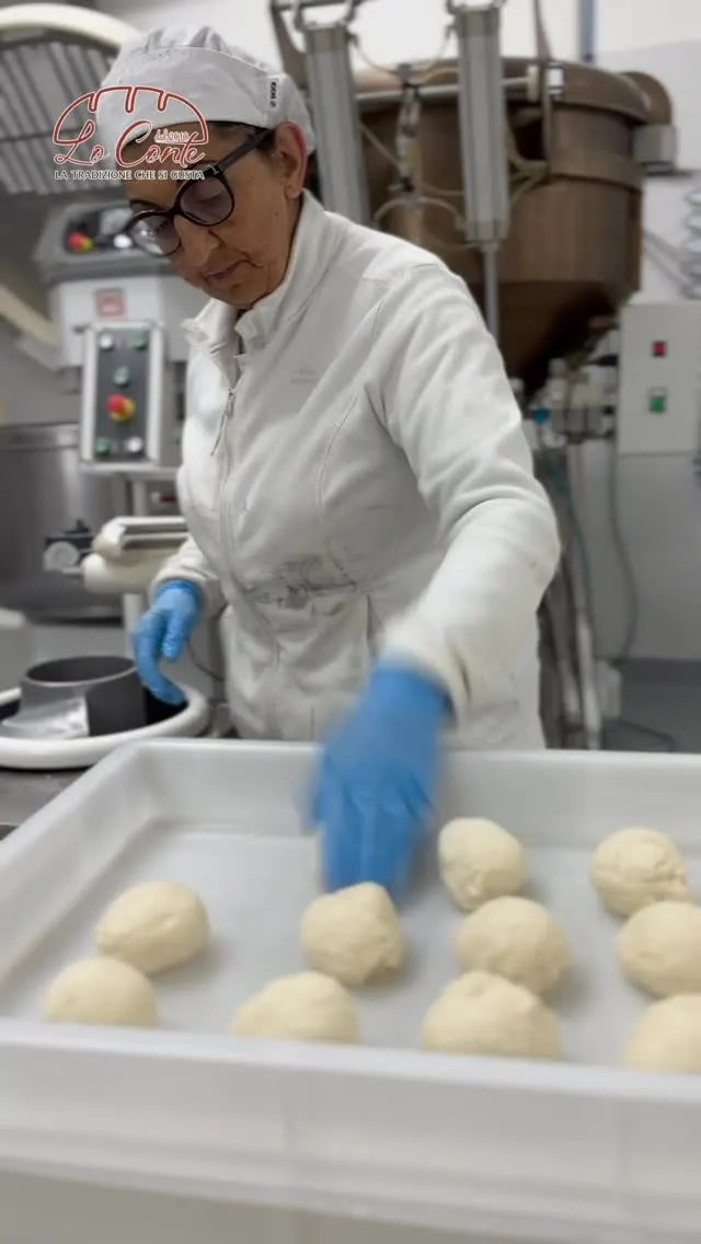 Una panettiera con la cuffia dispone i panetti di impasto nelle vaschette