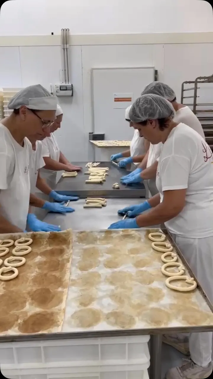 Operatrici con cuffia e guanti modellano i taralli a mano sui vassoi del laboratorio